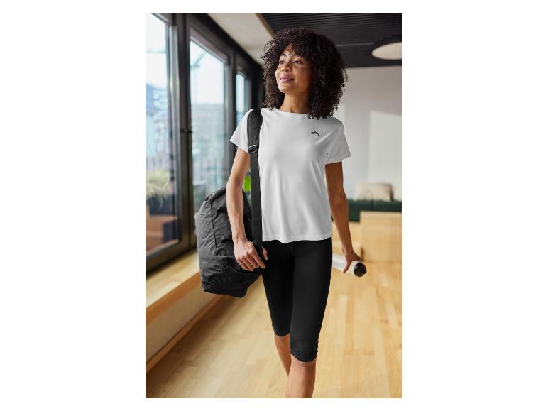 Vrouw in wit sportshirt en zwarte legging, met sporttas en waterfles.