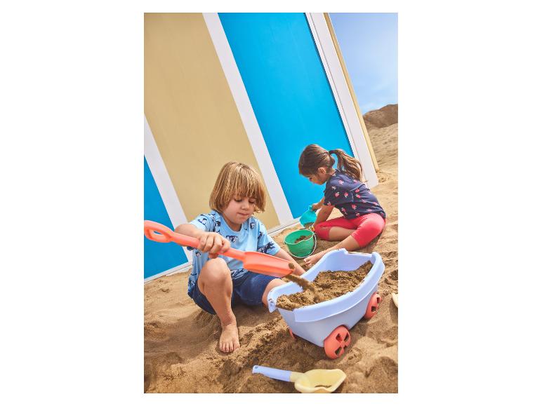 Twee kinderen spelen in het zand met strandspeelgoed, waaronder een kar en schepjes.