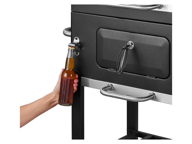 Een hand opent een bierflesje aan een zwarte grill met ingebouwde flesopener.