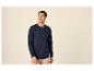 Man in een marineblauw shirt met lange mouwen en beige broek, lachend en naar rechts kijkend.