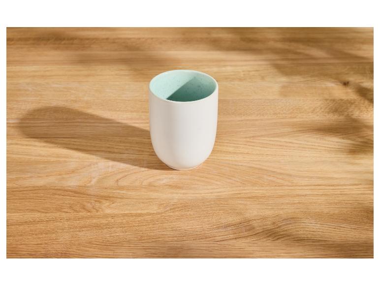 Witte keramische mok met lichtblauwe binnenkant op een houten tafel met schaduwen.