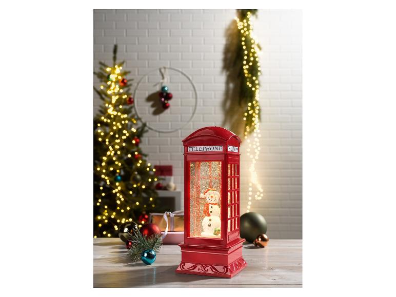 Een rode telefooncel sneeuwbol met een sneeuwpop erin, omringd door kerstversiering.