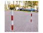 Twee rood-witte palen met een ketting op een geplaveide stoep, met auto's op de achtergrond.