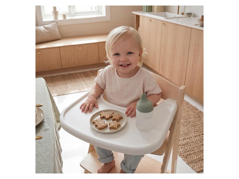 Lachende peuter in een houten kinderstoel met koekjes en een babyfles.
