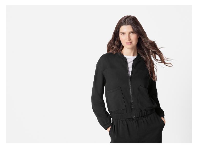 Een vrouw in een zwarte joggingbroek en een zwarte bomberjack.