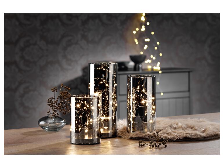 Drie glazen lantaarns met ingebouwde LED-verlichting, op een houten tafel.