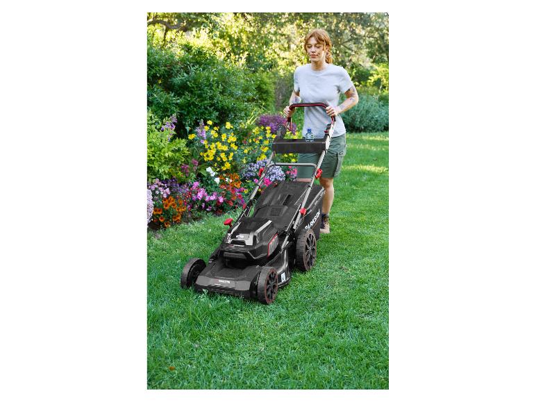 Vrouw maait gras met een Parkside grasmaaier in een bloeiende tuin.