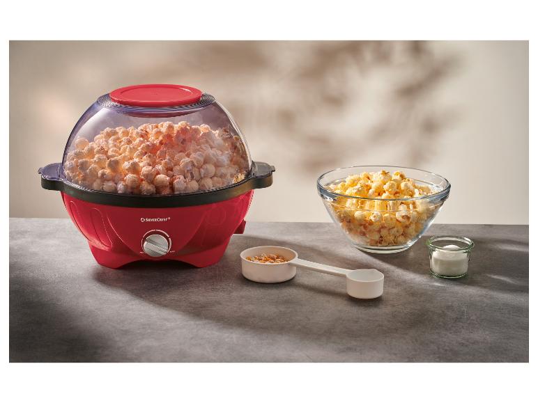 Rode popcornmachine vol popcorn, met een kom popcorn en ingrediënten op een tafel.