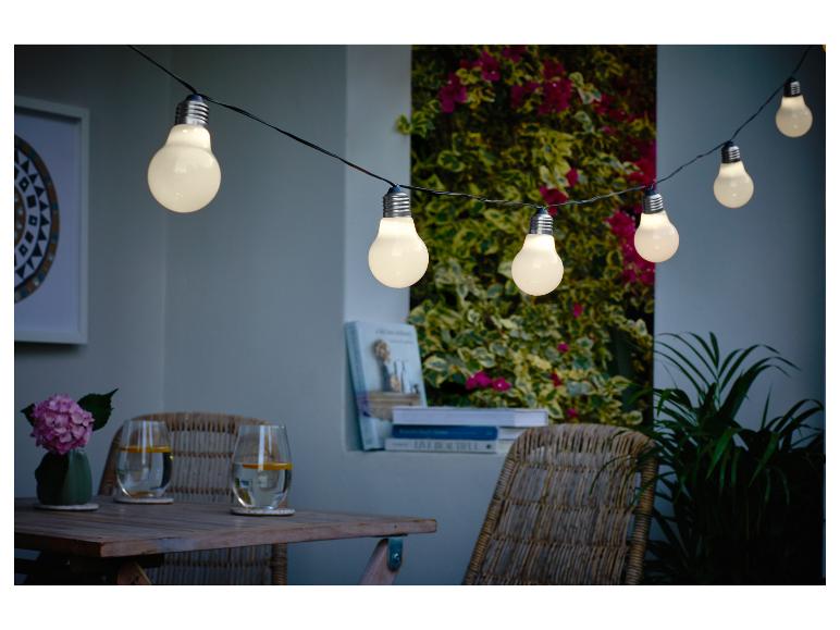 Buitenverlichting verlicht een gezellige patio met een houten tafel en rieten stoelen.