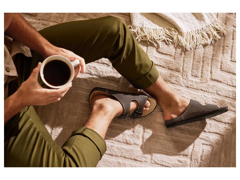 Man in olijfgroene broek en sandalen, drinkt koffie op een knusse deken.