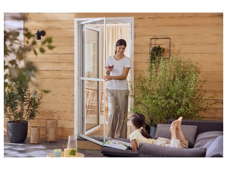 Vrouw met bessen opent een terrasdeur naar een meisje dat ontspant op tuinmeubelen.