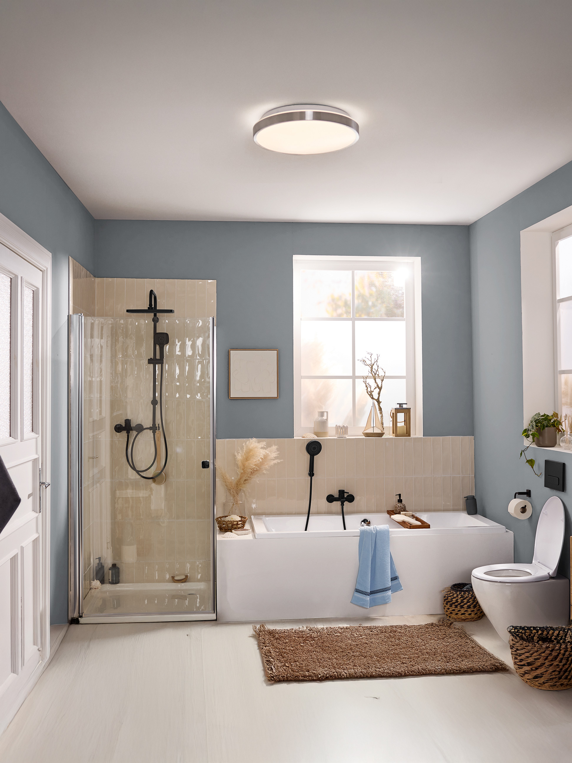 Moderne badkamer met blauwe muren, douchecabine, bad, toilet en ronde plafondlamp.