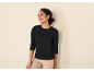 Vrouw in zwart shirt met lange mouwen en beige broek lacht, kijkt opzij.