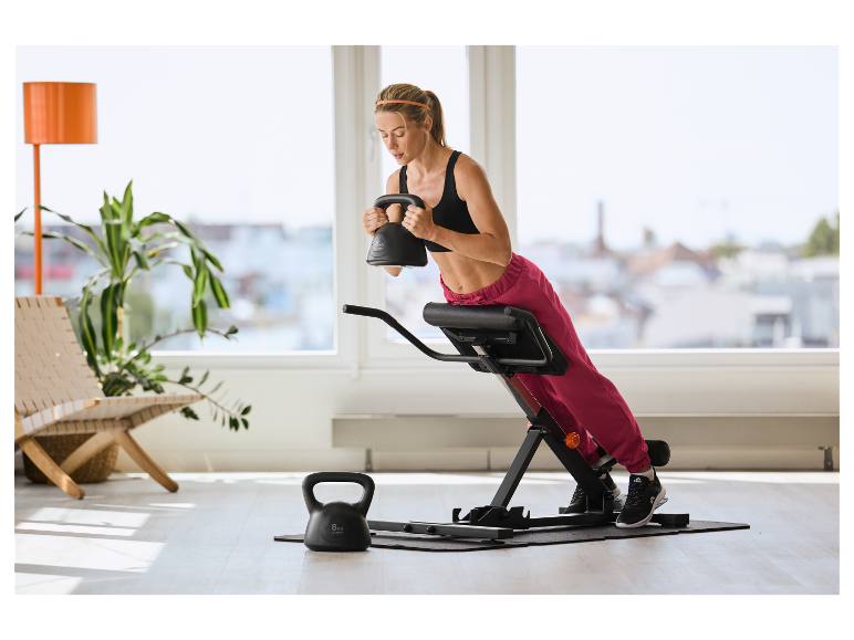 Vrouw traint met CRIVIT 6 kg kettlebell en rugtrainer.