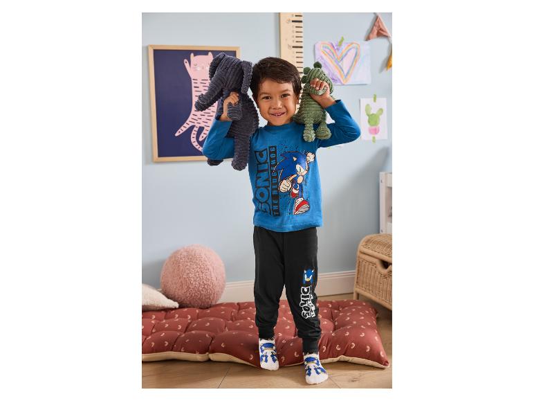 Lachende jongen in Sonic the Hedgehog pyjama met twee knuffels in een speelse kamer.