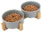 Twee grijze voerbakken met houten onderstellen, gevuld met hondenvoer.
