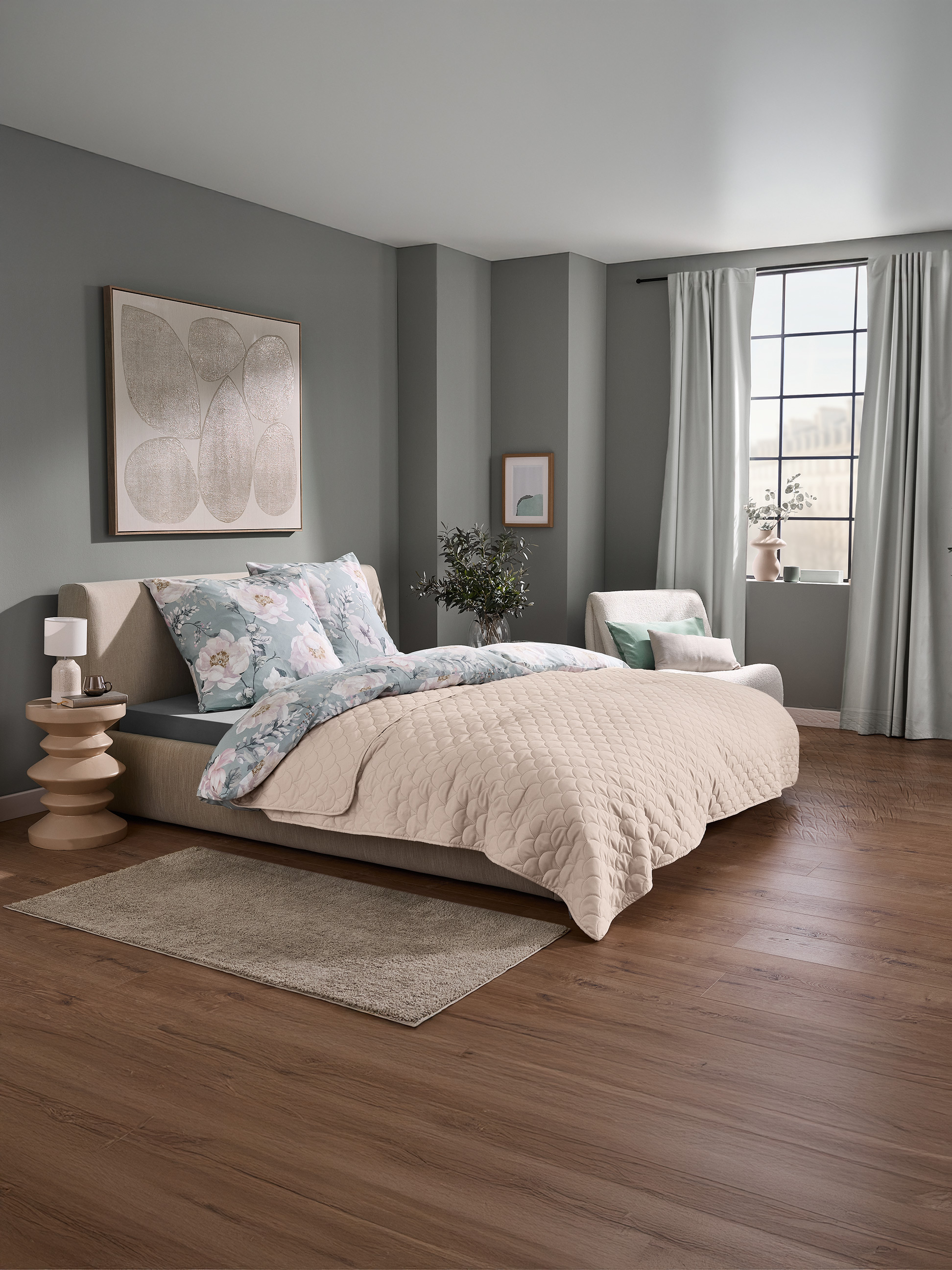 Slaapkamer met een bed met bloemig beddengoed en een beige gewatteerde sprei, en een raam met gordijnen.