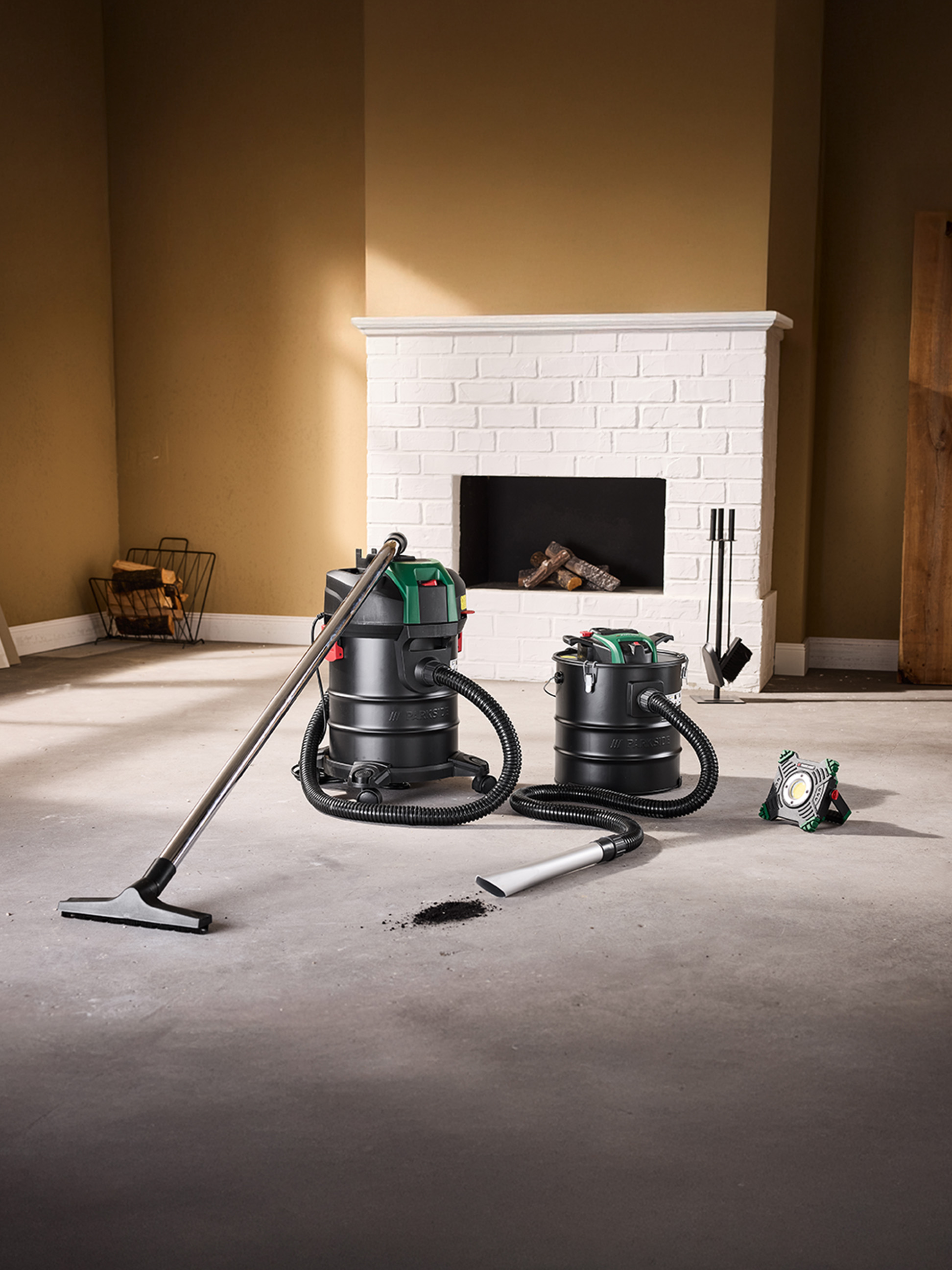 Twee aszuigers en een bouwlamp op een betonnen vloer voor een open haard.