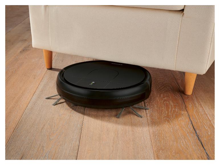 Zwarte robotstofzuiger onder een beige bank op een houten vloer.