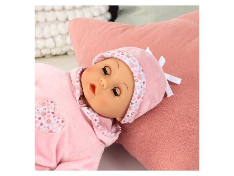 Een pop in roze pyjama en muts met hartjes en rozen, liggend op een roze kussen.