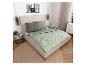 Slaapkamer met beige bed, groen beddengoed met bladpatroon en rond vloerkleed.
