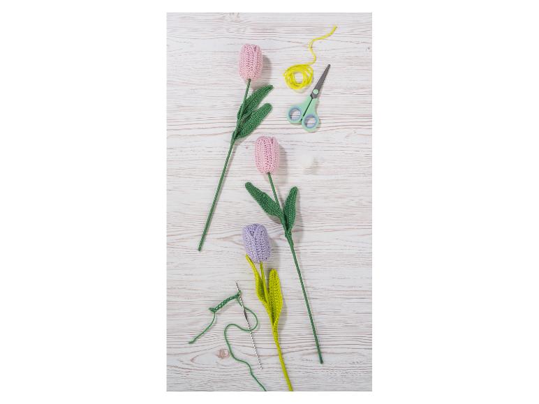 Roze en paarse gehaakte tulpen met garen, schaar en haaknaald op een houten tafel.