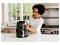 Vrouw in de keuken gebruikt een airfryer, lachend en kijkend naar het apparaat.