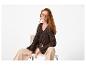 Vrouw in bruin gebreid vest en beige broek, zittend op een stoel.