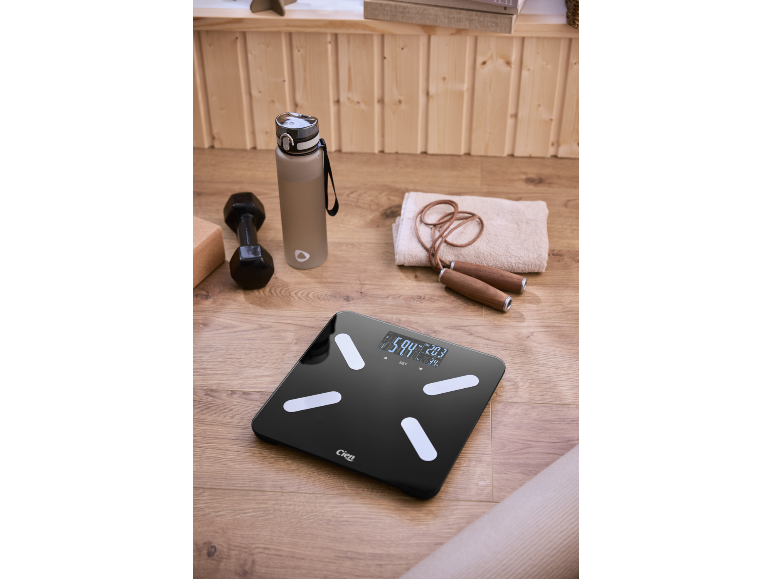 Digitale weegschaal op een houten vloer met fitnessaccessoires.