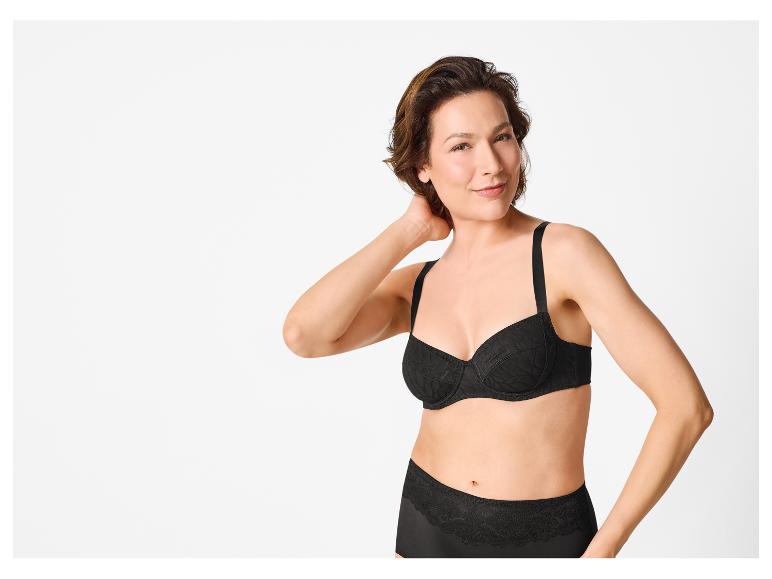 Vrouw in zwarte kanten beha en slip, lachend naar de camera.