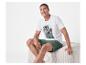 Man in wit T-shirt met palmprint en groene shorts zit op een poef.