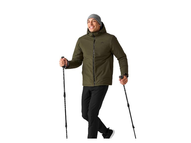 Een man in een groene jas en zwarte broek houdt twee trekkingstokken vast.