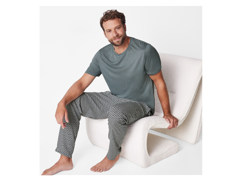 Man in donkergroen t-shirt en gepatroneerde broek zit op een pluizige stoel.
