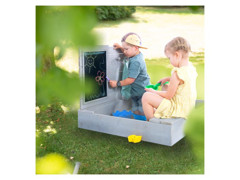 Twee kinderen spelen in een houten zandbak met een schoolbord.