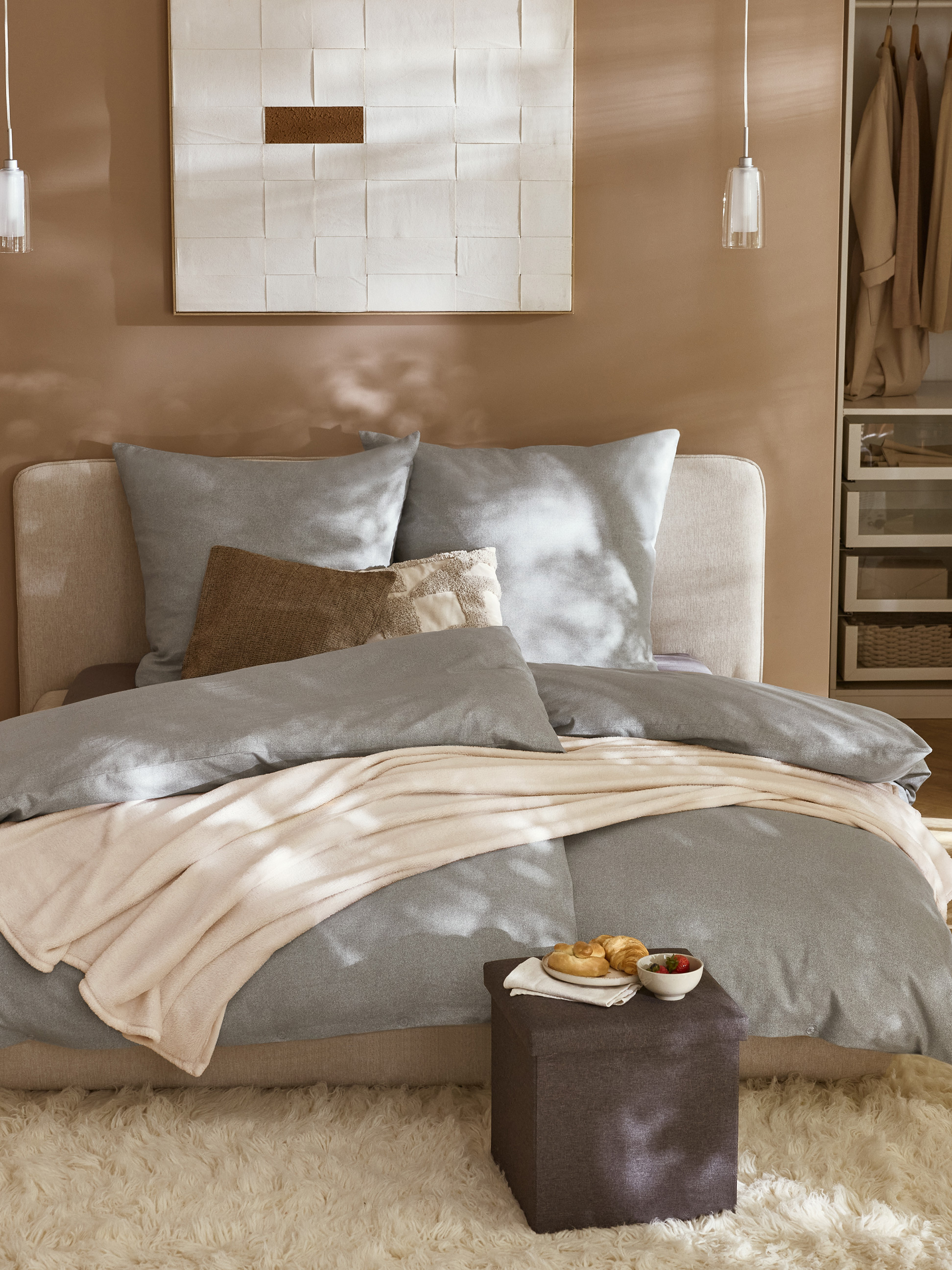 Gezellige slaapkamer met een grijs bed, beige plaid en bruine poef met ontbijt.