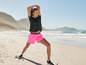 Een vrouw in roze shorts en een zwart shirt doet yoga op het strand.