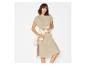 Vrouw in beige T-shirtjurk met een wit overhemd om de taille geknoopt.