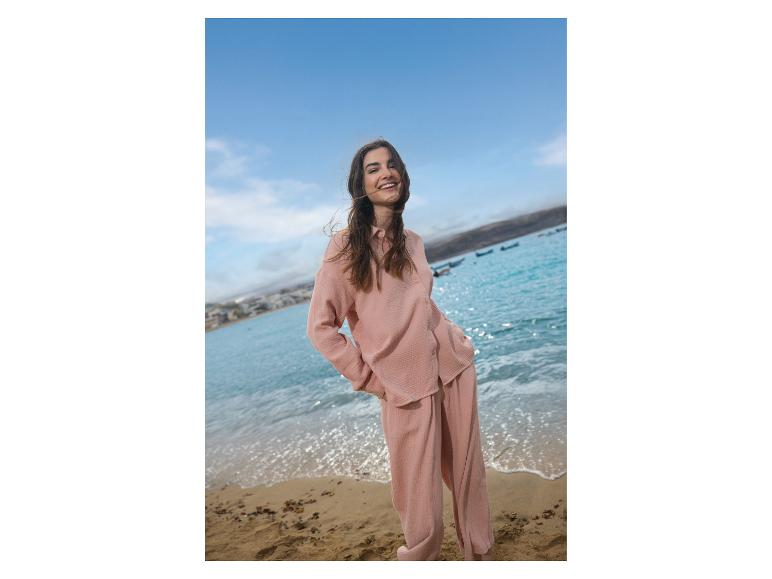 Lachende vrouw in roze pyjama op een zonnig strand.