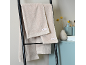 Beige handdoeken hangen aan een zwart ladderrek in een badkamer met lichtblauwe accenten.