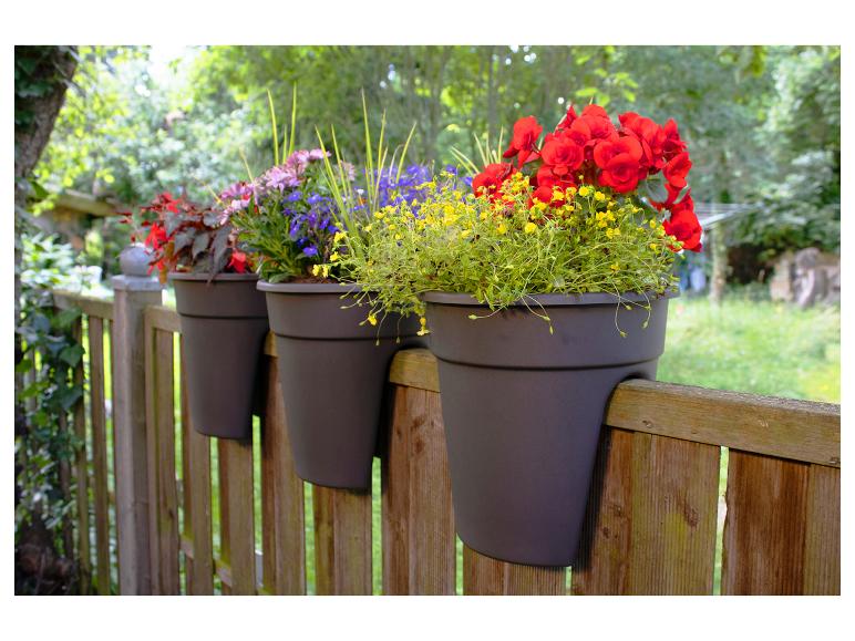 Drie grijze bloempotten met kleurrijke bloemen hangen aan een houten hek.