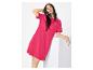 Vrouw in een fuchsia T-shirtjurk, leunend op een wit blok.