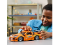Kind speelt met een oranje speelgoedraceauto op een tafel.