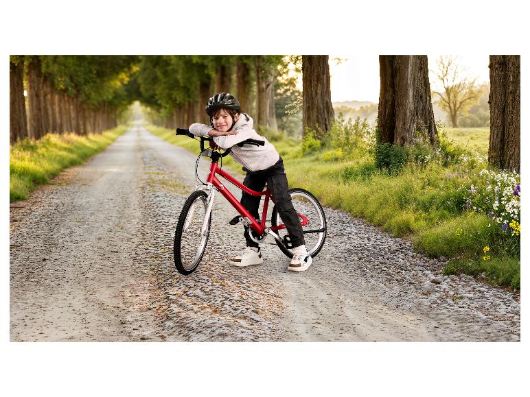 Jongen met helm en fiets op een landweg omringd door bomen.