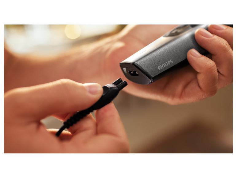 Handen sluiten een oplader aan op een grijs elektrisch scheerapparaat.