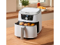 Witte airfryer met open lade waarin kipnuggets worden bereid, op een houten aanrecht.