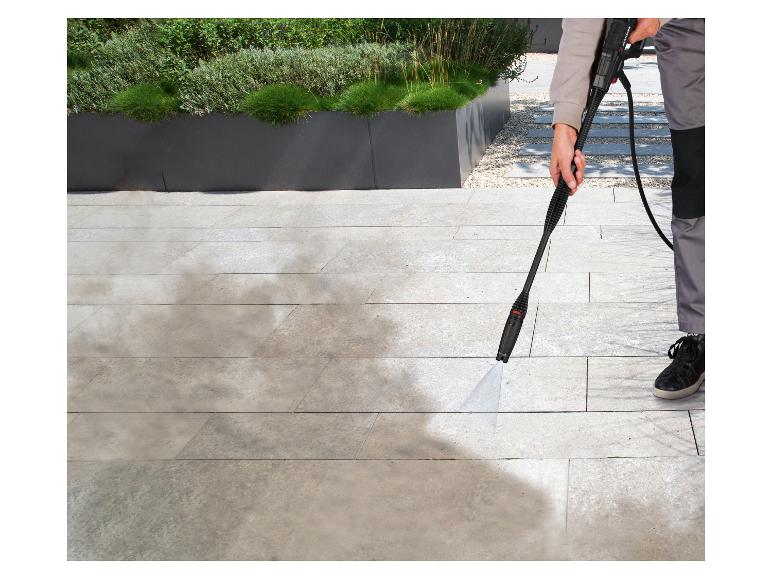 Persoon reinigt terras met hogedrukreiniger, verwijdert vuil van lichte tegels.