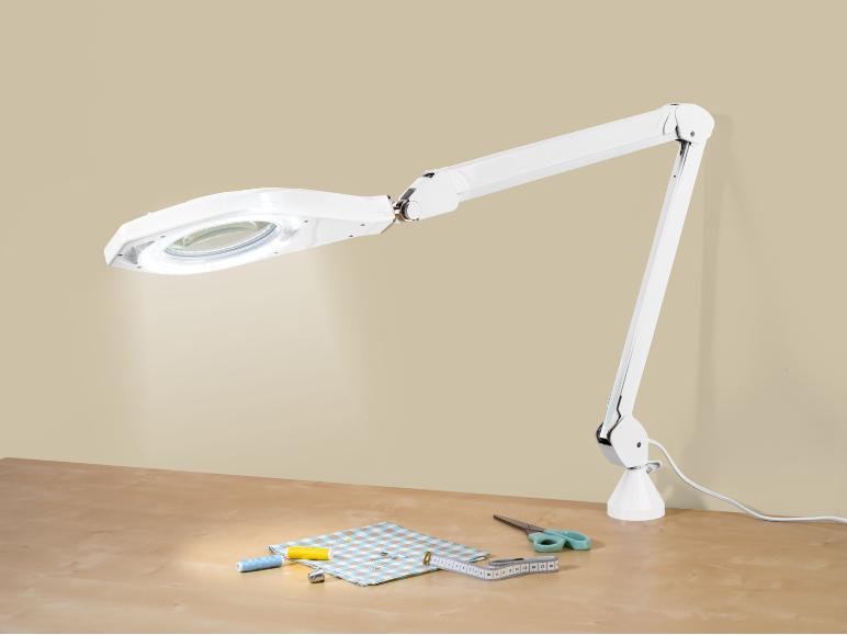 Witte vergrootlamp verlicht naaiartikelen op een houten tafel.
