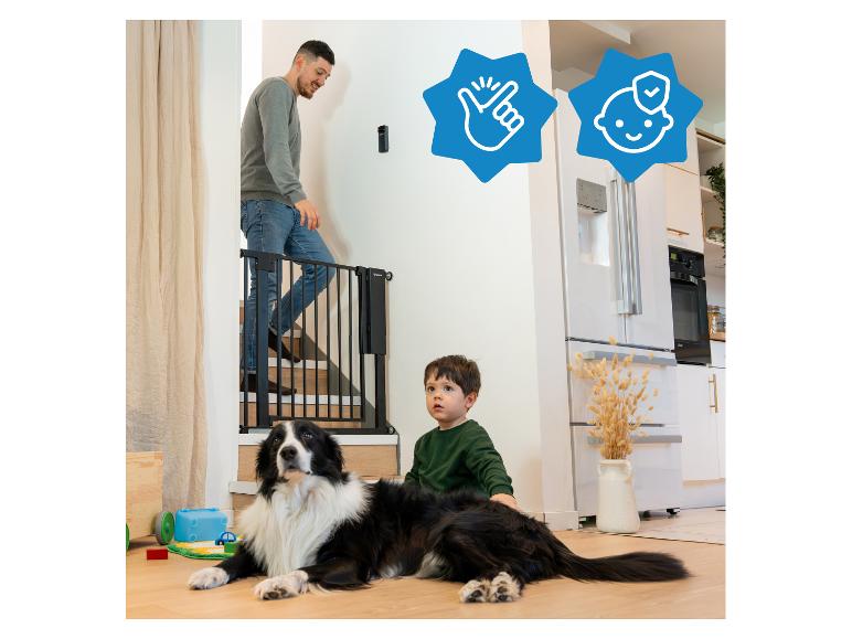 Man op trap, babyhekje, kind en hond in woonkamer, met koelkast in de keuken.