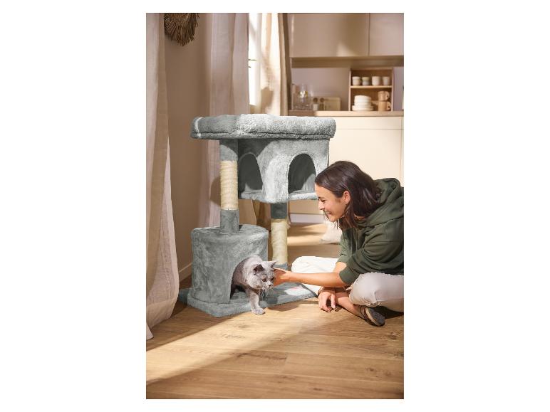 Vrouw aait kat in grijze krabpaal, keuken op de achtergrond.