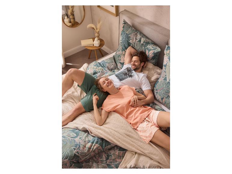 Koppel in tropische pyjama ontspant op een bed met een bedrukt dekbedovertrek.